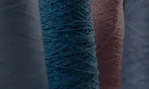 Gomitoli di filato color petrolio e rosa, pronti per creare maglioni pregiati.