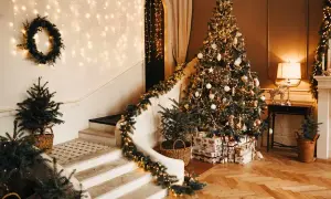 Un albero di Natale scintillante, decorato con nastri natalizi per albero, addobbi dorati e luci calde. La scala è adornata da ghirlande luminose e piccoli abeti in cesti.