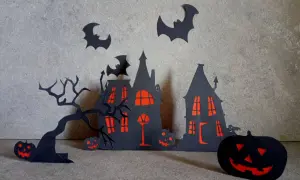 Scena di Halloween fai da te con case infestate, alberi spogli, pipistrelli e zucche intagliate.
