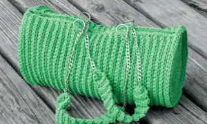 Borsa verde brillante lavorata all'uncinetto doppia punta, con manici e catene argentate, adagiata su assi di legno.