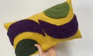 Cuscino rettangolare giallo con motivi astratti in microspugna viola e verde.