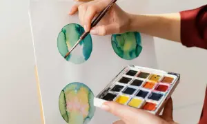 Mano che dipinge cerchi verdi e gialli con acquerello su tela. Palette di colori in primo piano.