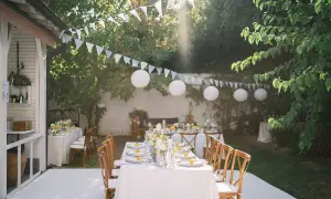Tavoli apparecchiati in giardino per un evento, con festoni e lanterne. I **fogli di caucciù** sono assenti, ma l'atmosfera è festosa.