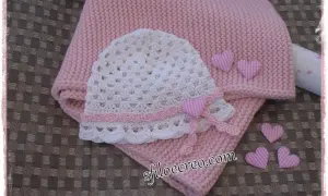 Schema maglia uncinetto bambina: cappellino bianco traforato e copertina rosa, decorati con cuoricini a quadretti.