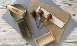 Attrezzi per la stampa linoleum: sgorbie, rullo, tavoletta di linoleum e carta.