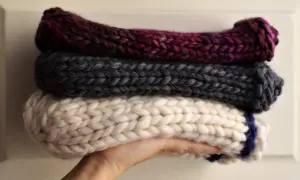 Tre berretti in lana ai ferri, uno bordeaux, uno grigio e uno bianco con striscia blu, impilati su una mano.