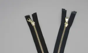 Due cerniere lampo eleganti nere con dettagli dorati su sfondo grigio.