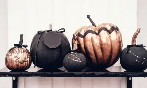 Cinque zucche decorate per Halloween: una colorata con "Trick or Treat", una grande color bronzo, e tre nere con disegni di costellazioni.