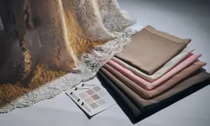 Tessuti pregiati: un drappo di pizzo dorato e avorio accanto a campioni di tessuti color carne, rosa e grigio.