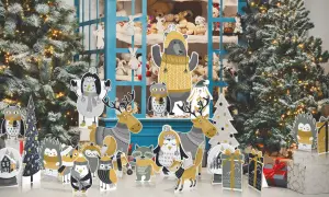 Sagome natalizie grandi di animali e alberi, con un orso al centro, davanti a un albero di Natale innevato e una vetrina piena di peluche.