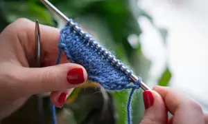 Mani con unghie rosse lavorano a maglia un filato blu. Impara come lavorare la lana con questo dettaglio ravvicinato.