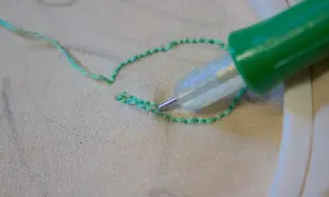 Ago magico crea schemi su stoffa, un punto alla volta, con filo verde brillante.