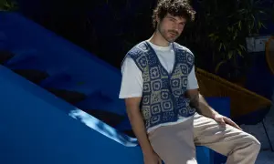 Uomo con riccio gilet senza maniche all'uncinetto blu e beige, seduto su una struttura blu.