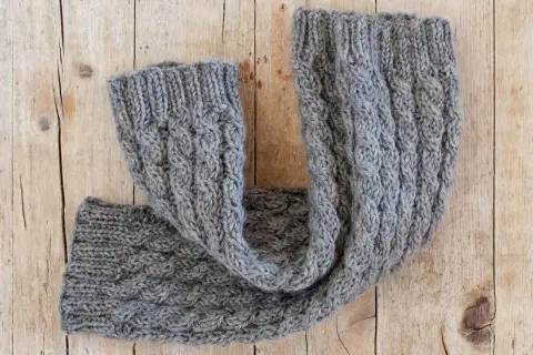 Un caldo scaldacollo grigio lavorato a maglia con trecce. Perfetto per scoprire cosa fare con 100 grammi di lana.