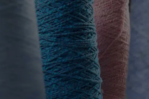 Gomitoli di filato color petrolio e rosa, pronti per creare maglioni pregiati.