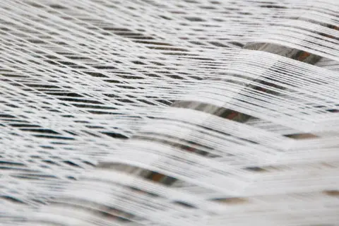 Fili bianchi di cotone organico intrecciati, creando un motivo a rete morbido e naturale.