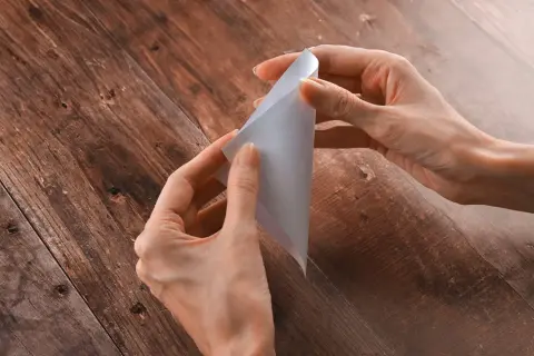 Mani che creano una pieghetta su un foglio di carta bianca, su un tavolo di legno scuro.