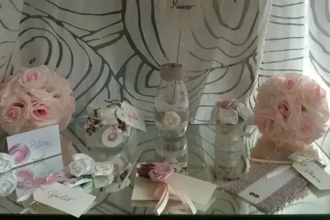Segnaposto matrimonio fai da te shabby chic: rose rosa e bianche, vasetti decorati con pizzo, biglietti con nomi.