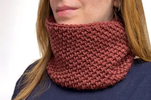 Donna con scaldacollo fai da te color mattone, lavorato a maglia, che le scalda il collo.
