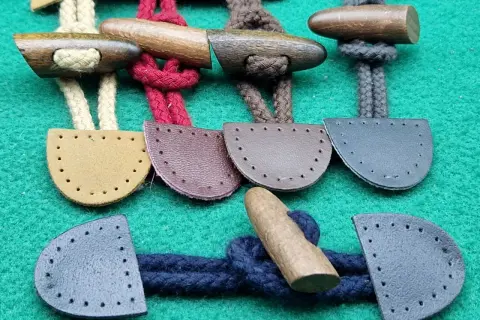 Bottoni alamari fai da te in legno e pelle, pronti per essere cuciti su capi d'abbigliamento.