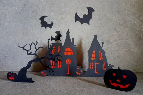 Scena di Halloween fai da te con case infestate, alberi spogli, pipistrelli e zucche intagliate.