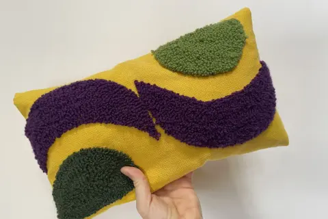 Cuscino rettangolare giallo con motivi astratti in microspugna viola e verde.