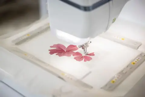 Macchina da cucire ricama un fiore rosso su un sottile tulle materiale.
