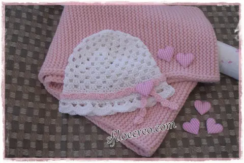 Schema maglia uncinetto bambina: cappellino bianco traforato e copertina rosa, decorati con cuoricini a quadretti.