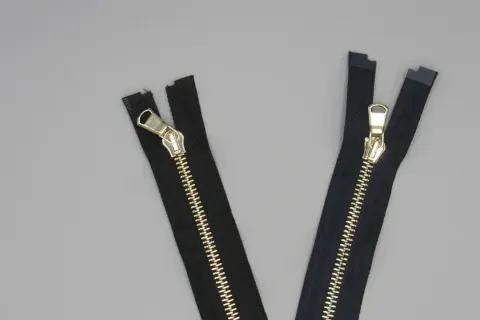 Due cerniere lampo eleganti nere con dettagli dorati su sfondo grigio.