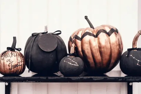 Cinque zucche decorate per Halloween: una colorata con "Trick or Treat", una grande color bronzo, e tre nere con disegni di costellazioni.