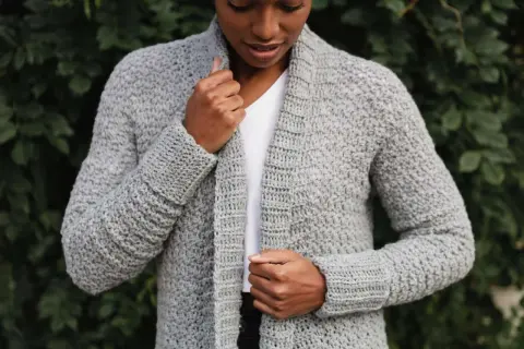 Donna con cardigan grigio all'uncinetto, perfetto per chi cerca schemi gratis per creare capi unici.