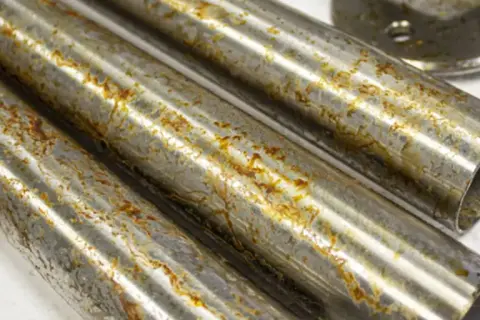 Tubi di acciaio inossidabile con macchie di ruggine marrone e giallastre, che suggeriscono come l'acciaio inossidabile diventa nero con il tempo e l'esposizione.