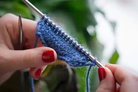 Mani con unghie rosse lavorano a maglia un filato blu. Impara come lavorare la lana con questo dettaglio ravvicinato.