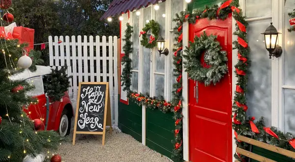 Un angolo magico per idee per mercatini di natale fai da te: un albero addobbato, una lavagna con "Happy New Year" e una casetta decorata a festa.