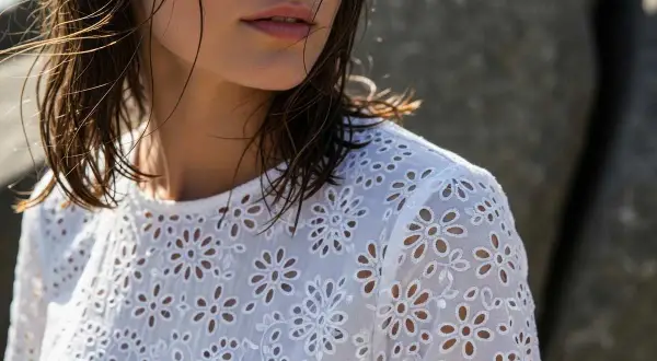 Dettaglio di una donna con capelli bagnati che indossa una blusa bianca con un delicato pizzo di San Gallo.