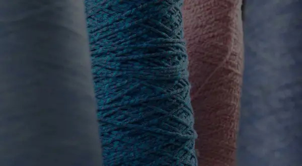 Gomitoli di filato color petrolio e rosa, pronti per creare maglioni pregiati.