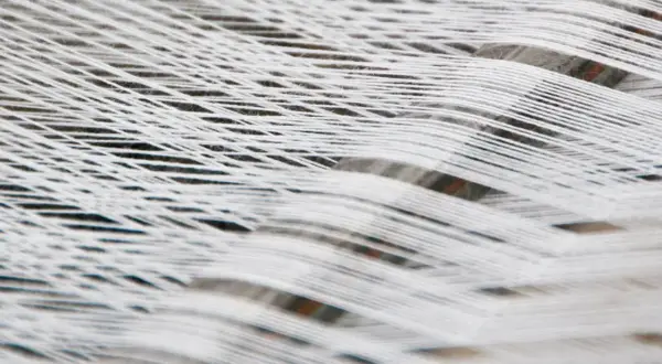 Fili bianchi di cotone organico intrecciati, creando un motivo a rete morbido e naturale.