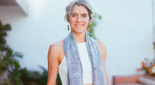 Donna sorridente con sciarpa grigia, un esempio di quanto deve essere lunga una sciarpa da donna per un look casual e chic.