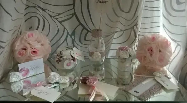 Segnaposto matrimonio fai da te shabby chic: rose rosa e bianche, vasetti decorati con pizzo, biglietti con nomi.