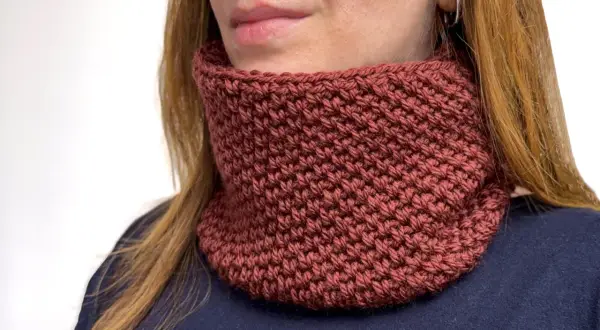 Donna con scaldacollo fai da te color mattone, lavorato a maglia, che le scalda il collo.