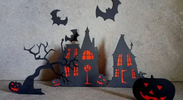 Scena di Halloween fai da te con case infestate, alberi spogli, pipistrelli e zucche intagliate.