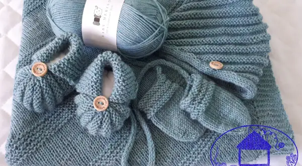 Un set per neonato ai ferri: copertina, scarpine e cappellino in lana merino azzurra, con bottoncini in legno.