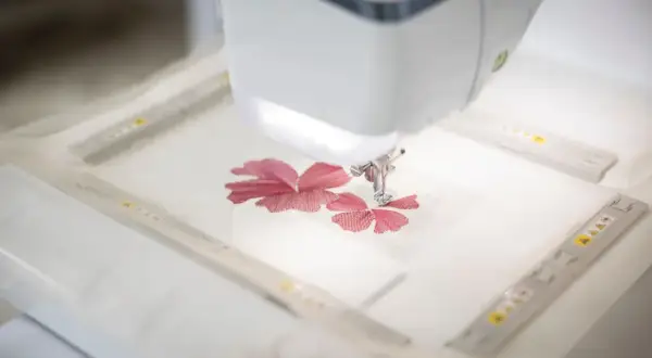 Macchina da cucire ricama un fiore rosso su un sottile tulle materiale.