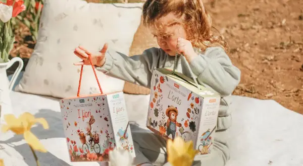 Bambina con due scatole di puzzle ad acqua, perfetti per le attività estive. Un coniglietto in bici e un orsetto giardiniere animano i giochi.