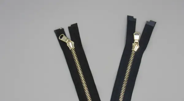 Due cerniere lampo eleganti nere con dettagli dorati su sfondo grigio.