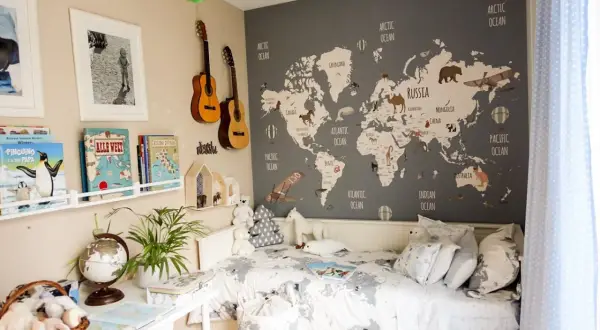 Camera da letto con mappa del mondo e decorazioni tema viaggio: aerei, mongolfiere, animali e chitarre.