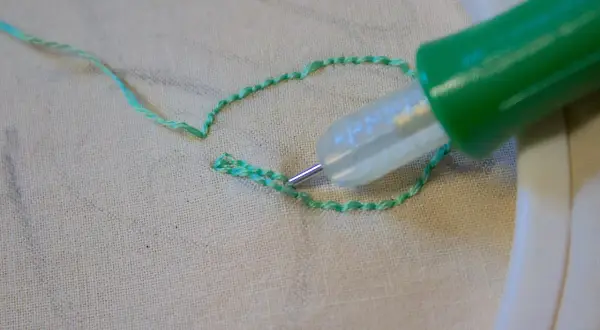 Ago magico crea schemi su stoffa, un punto alla volta, con filo verde brillante.