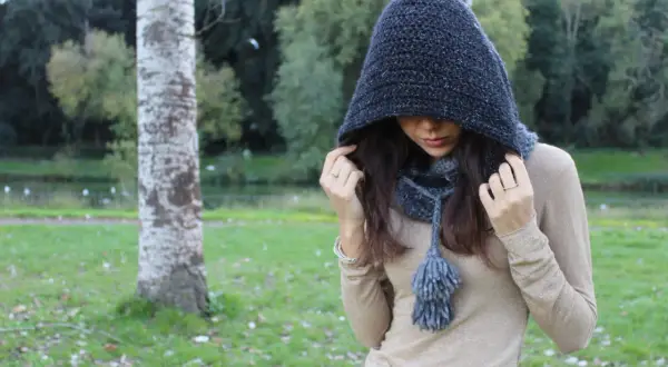 Donna con scaldacollo con cappuccio ai ferri, in un parco autunnale.