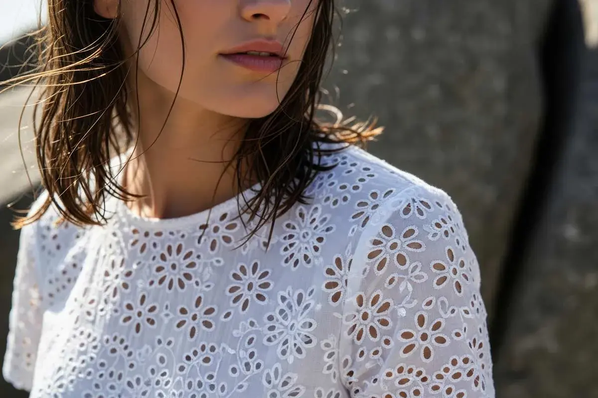 Dettaglio di una donna con capelli bagnati che indossa una blusa bianca con un delicato pizzo di San Gallo.
