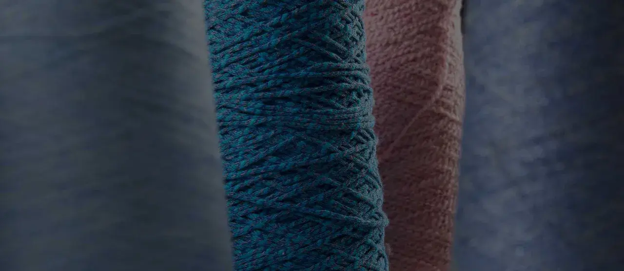 Gomitoli di filato color petrolio e rosa, pronti per creare maglioni pregiati.